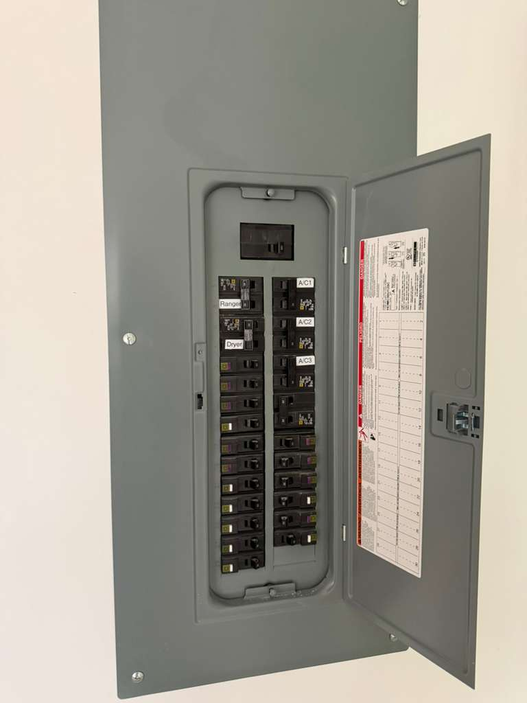 Electrical panel with multiple circuit breakers, including labels for Range, Dryer, and AC units. The panel door is open, showing the internal components and a diagram on the inside of the door.
