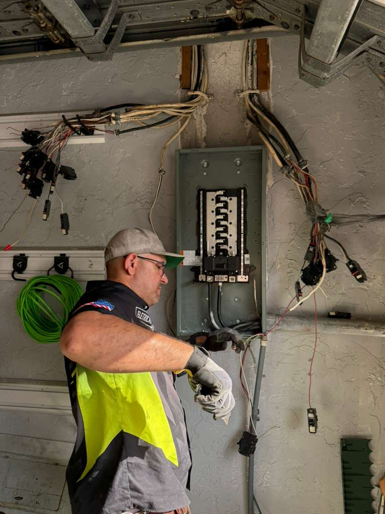 An electrician installing a new electrical panel or upgrading an existing one. There are many wires and breakers visible.