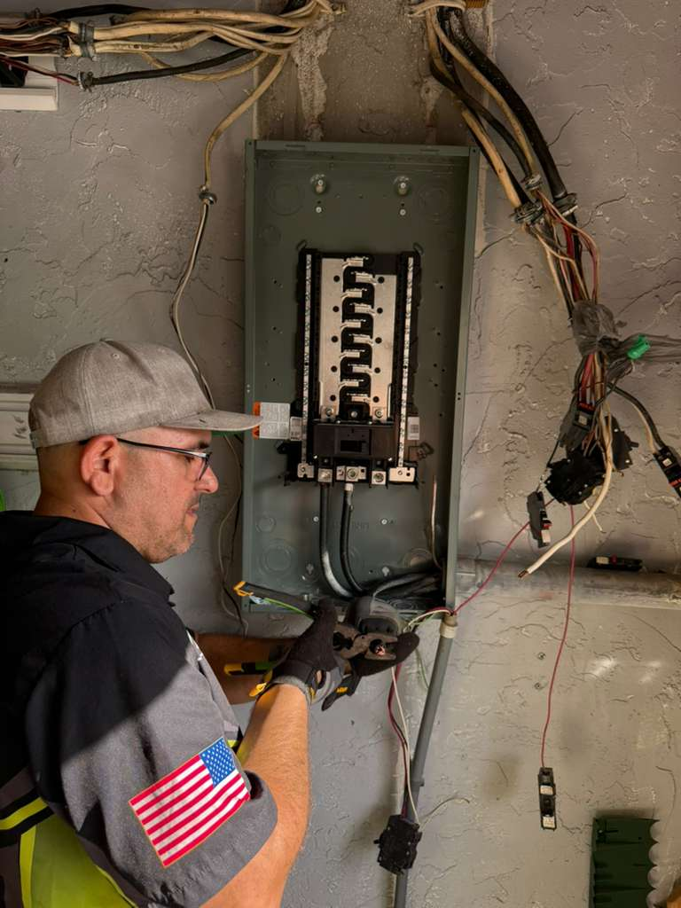 An electrician is working on a panel upgrade, connecting wires to a new circuit breaker panel.