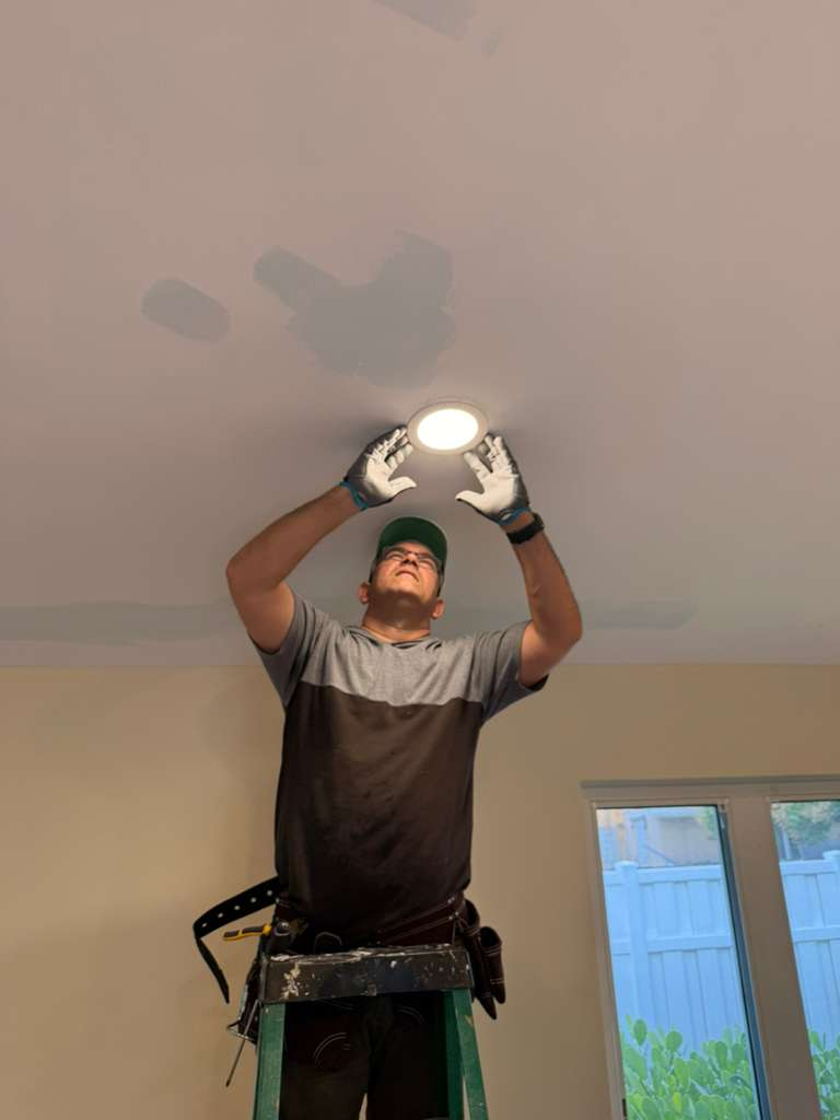 A worker on a ladder installing a recessed light fixture into a ceiling.