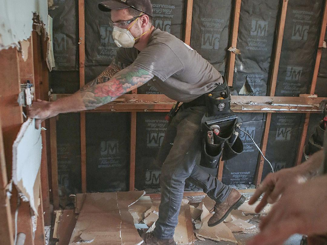 Worker tearing down drywall and exposing insulation during an interior demolition project.